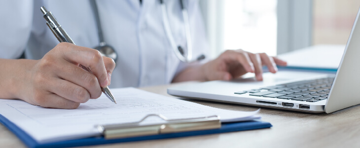 doctor using laptop and writing on a clipboard health insurance